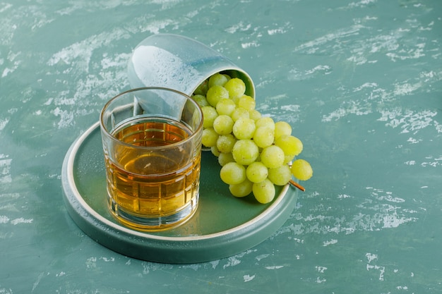 Free photo grapes with drink in a cup on plaster and tray background, high angle view.