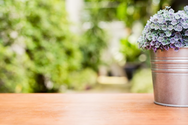 Free photo green plant in a flower pot on a wooden desk at the in front of house with blurred garden view textured background.