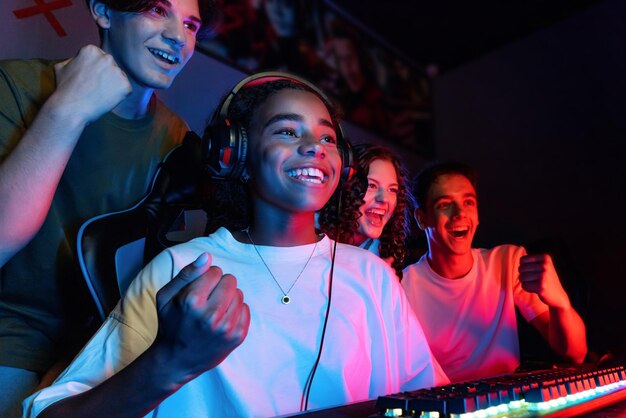 Group of multiracial teens playing video games in video game club with blue and red illumination Excited because of a victory