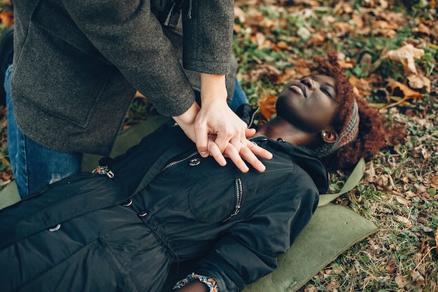 Foto gratuita guy aiuta una donna. la ragazza africana sta mentendo inconscia. fornire il primo soccorso nel parco.