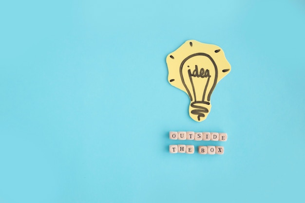 Free photo hand drawn idea light bulb outside the box text made with blocks on blue background