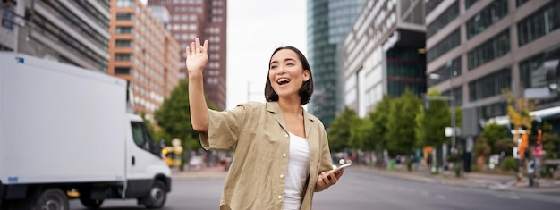 Free Photo happy asian girl passing by friend and waving at them on street saying hello while walking in city