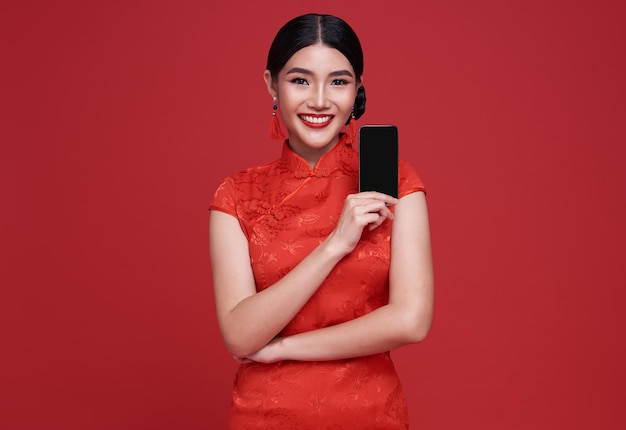 Free Photo happy asian woman wearing traditional cheongsam qipao dress showing mobile phone isolated on red background.