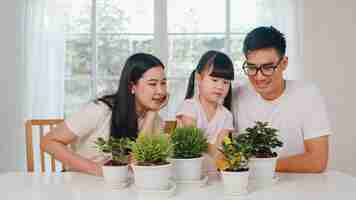 Free photo happy cheerful asian family dad, mom and daughter watering plant in gardening near window at house