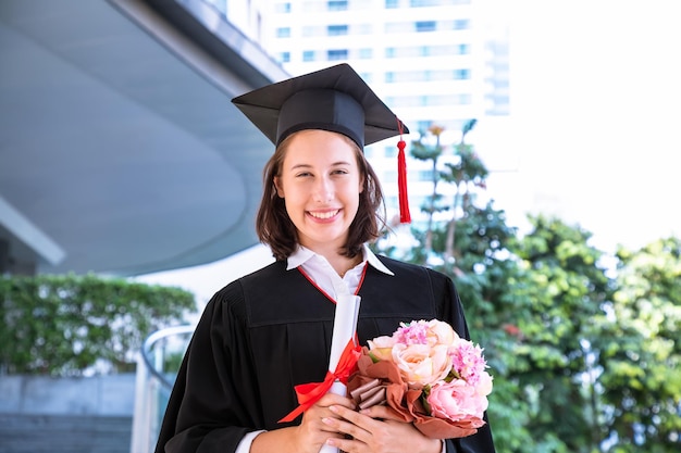 Free photo happy graduate student in ceremony with graduation gown certificate and flower