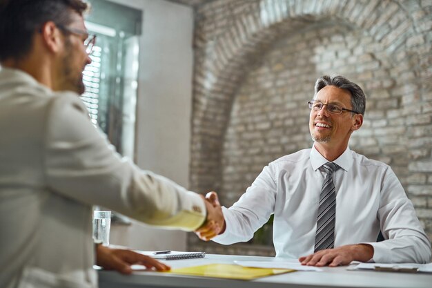 Happy manager handshaking with a candidate after successful job interview in the office