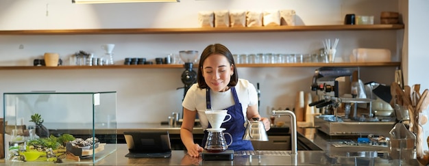 Free photo happy smiling asian girl smelling coffee while brewing filter standing behind counter in cafe