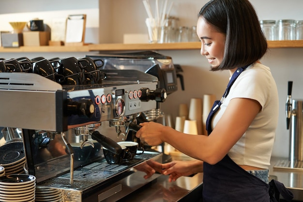 Free photo happy smiling bartender barista using coffee machine prepare order making cappuccino or latte wearin