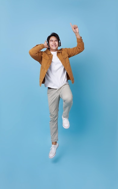 Free Photo happy young asian man listening music with headphone dancing and jumping isolated on blue background