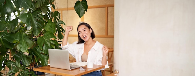 Free Photo happy young asian woman winning on laptop receive good news achieve goal at work triumphing and