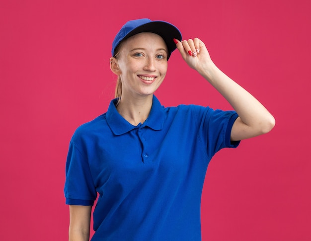 Free Photo happy young delivery girl in blue uniform and cap   smiling confident