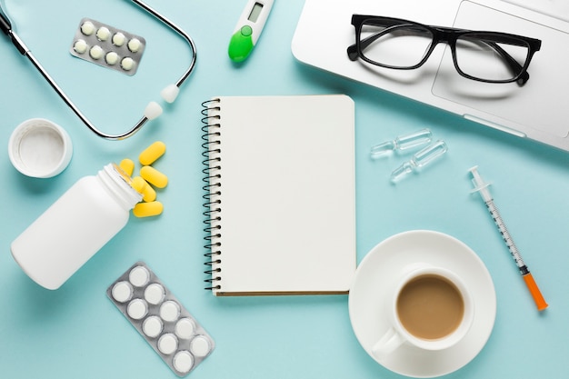 Free photo healthcare supplies with notepad; cup of coffee and spectacles on laptop over table