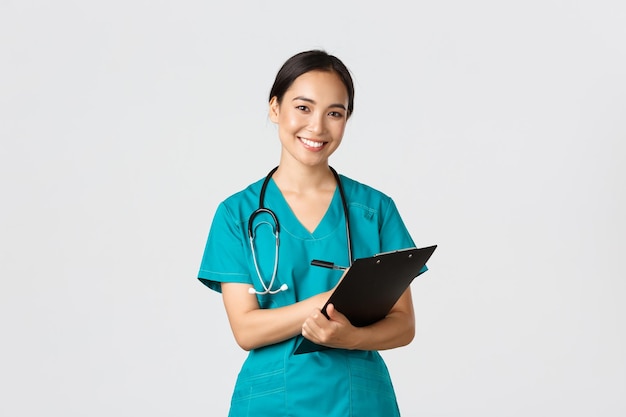 Free photo healthcare workers preventing virus quarantine campaign concept cheerful friendly asian female physician doctor with clipboard during daily checkup standing white background