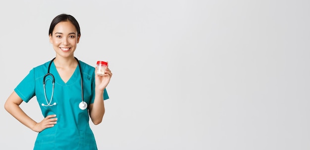 Free photo healthcare workers, preventing virus, quarantine campaign concept. smiling pretty asian female physician, nurse in scrubs showing pills, recommend medication or vitamins, white background.