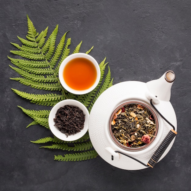 Free photo herbal tea with dried herb and fresh fern leaves on black slate backdrop