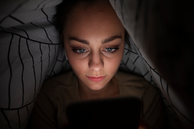 High angle girl with smartphone under blanket