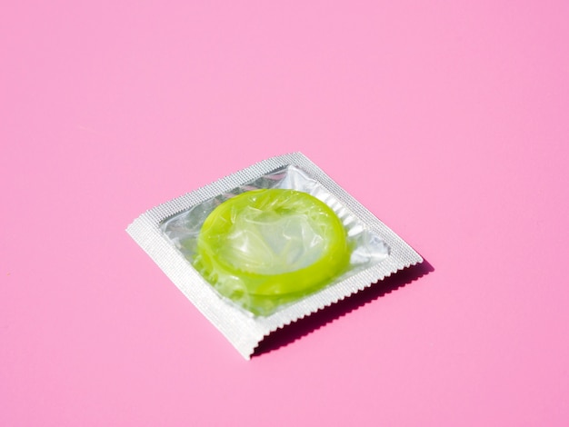 Free photo high angle green condom on pink background