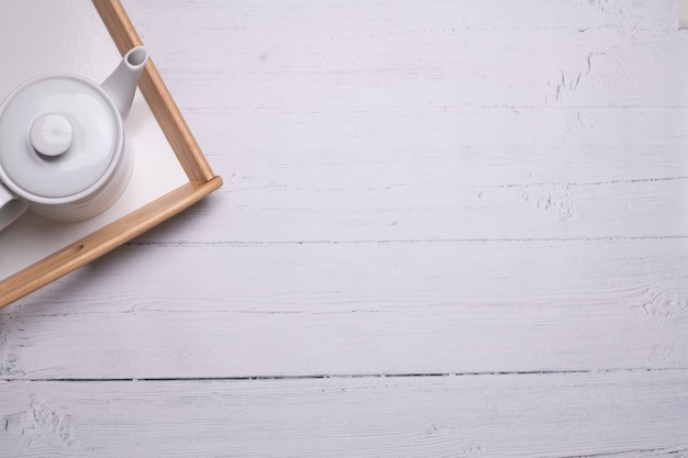 Free photo high angle shot of a white teapot on a tray on a white wooden table