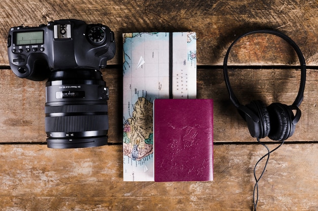 High angle view of Map, passport, headphone and DSLR camera on wooden background