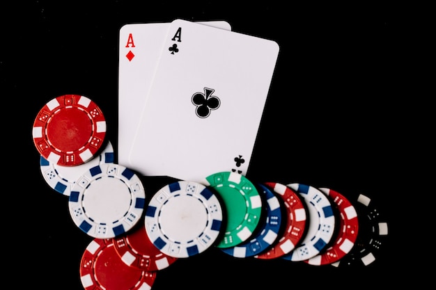 Free photo high angle view of poker chips and two aces playing cards on black backdrop