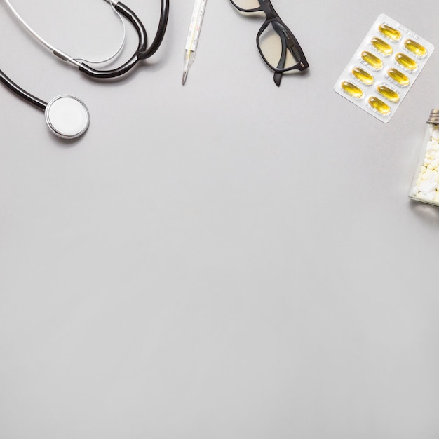 Free Photo high angle view of spectacles; thermometer; stethoscope and pills on grey background