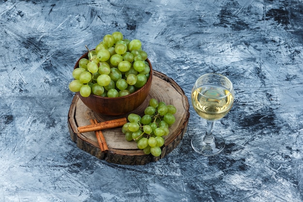 Free photo high angle view white grapes, cinnamon on wooden board with glass of whisky on dark blue marble background. horizontal