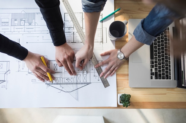 High angle view of worker's hand working on blueprint over wooden table at workplace