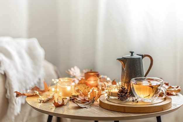 Free photo home autumn composition with tea, dry leaves and burning candles on blurred background, copy space.