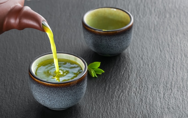 Free photo hot green tea is poured from the teapot into the blue bowl