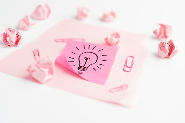 Free photo idea icon on adhesive note with paperclip; crumpled paper and card paper over white desk