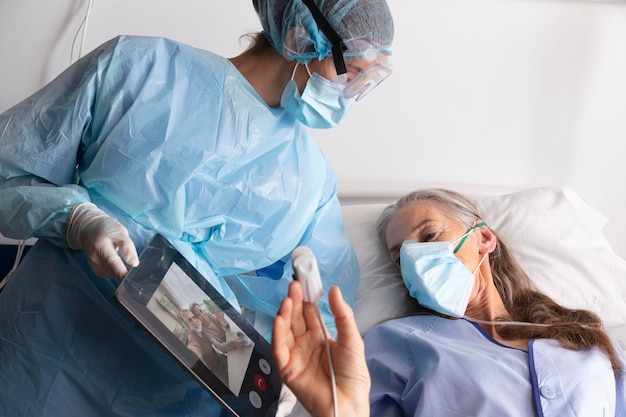 Free photo ill female patient in bed at the hospital talking to family through a tablet