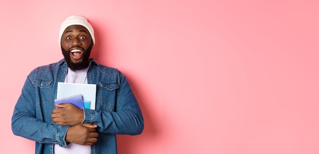 Free Photo image of adult africanamerican man holding notebooks and smiling studying at courses standing over p