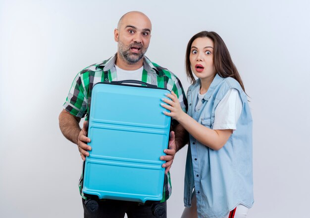 Free photo impressed adult traveler couple man holding suitcase and woman putting hand on suitcase both looking