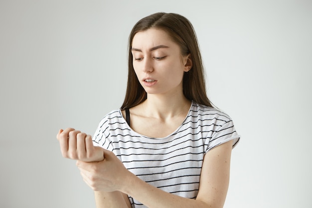 Free photo isolated picture of worried young european woman with dark loose hair holding hand at her wrist while checking pulse preassure after morning workout, having focused serious facial expression