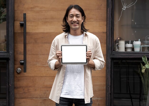 Free photo japanese man showing a digital tablet screen outside his sh