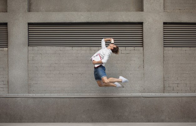 Jumping young buinessman in front of buildings, on the run in jump high