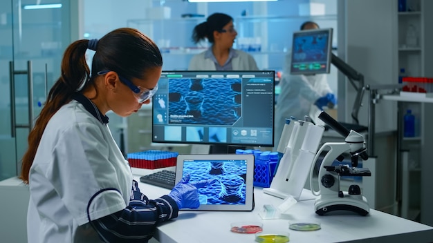 Free photo lab technician doctor analyzing virus evolution looking on digital tablet. team of scientists conducting vaccine development using high tech for researching treatment against covid19 pandemic.