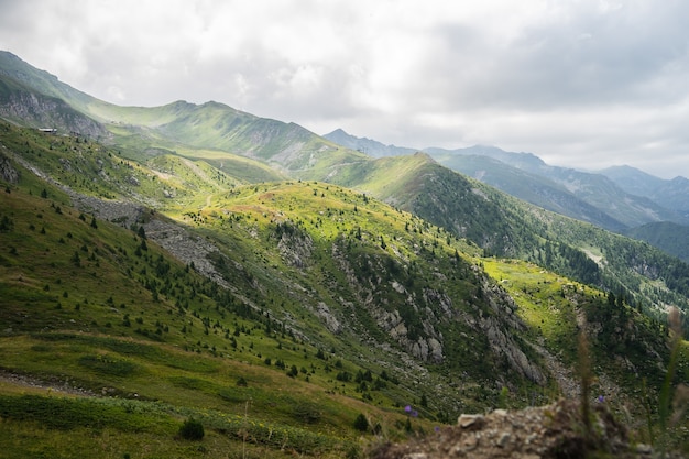 Бесплатное фото Пейзаж холмов, покрытых зеленью, со скалистыми горами под пасмурным небом на заднем плане