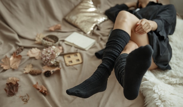 Free photo legs of a girl in warm knitted stockings in a cozy bed among the autumn leaves.