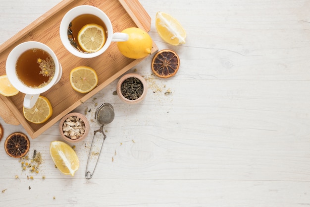 Free Photo lemon tea with lemons in tray and herbs on white wooden table