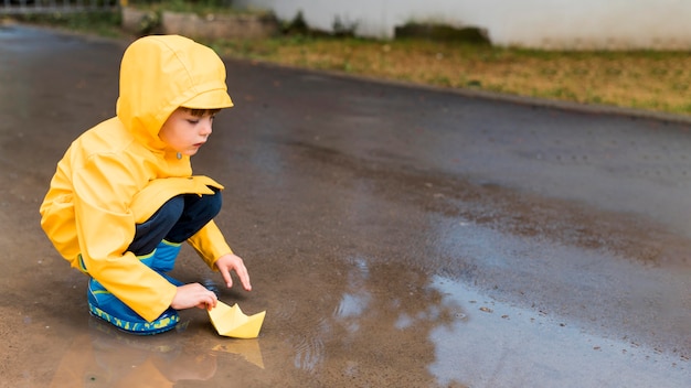 Free Photo little boy playing with a paper boat with copy space