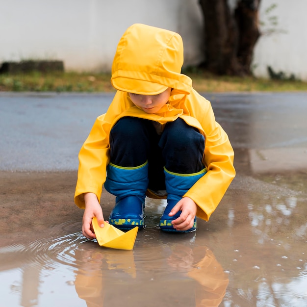 Free Photo little boy playing with a yellow paper boat