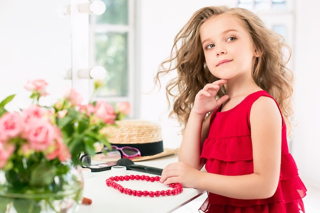 Free photo a little girl with cosmetics. she is in mother's bedroom, sitting near the mirror.