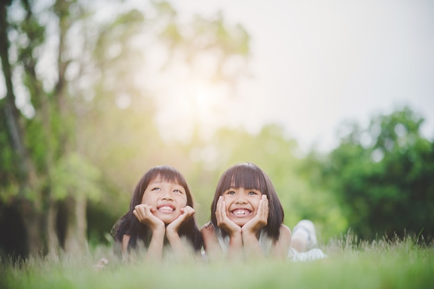 Free photo little girl with friend lying comfortably on the grass and smiling