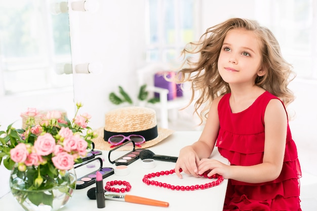 Free photo a little girl with red dress and cosmetics.