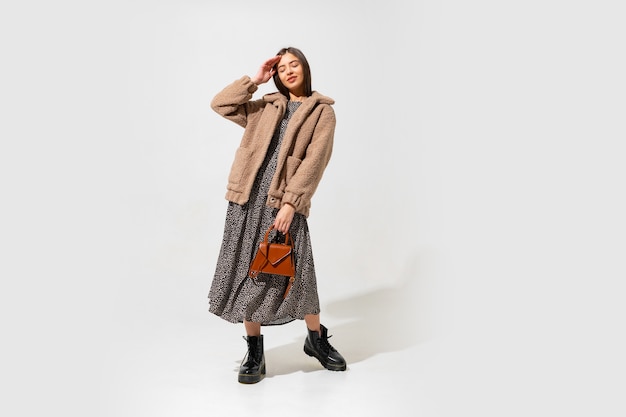 Free photo lovely european model in stylish fur coat and dress . wearing ankle boot in black leather. holding brown handbag.