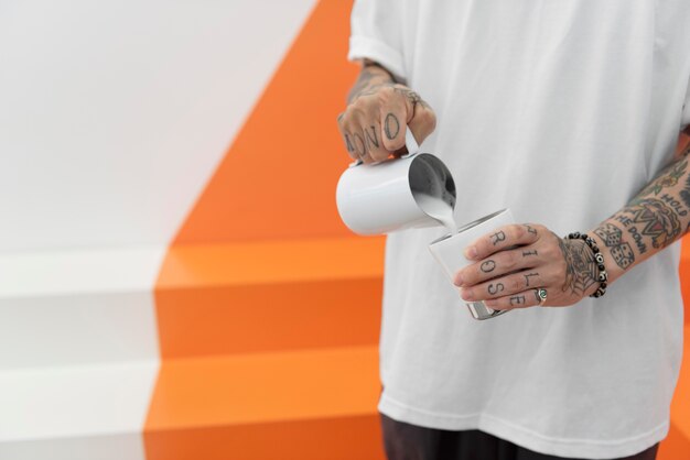 Male barista with tattoos adding milk to coffee