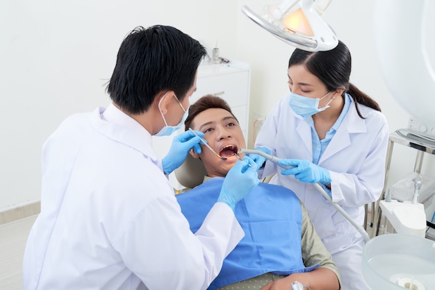 Free photo male dentist and nurse examining asian patient's teeth at clinic