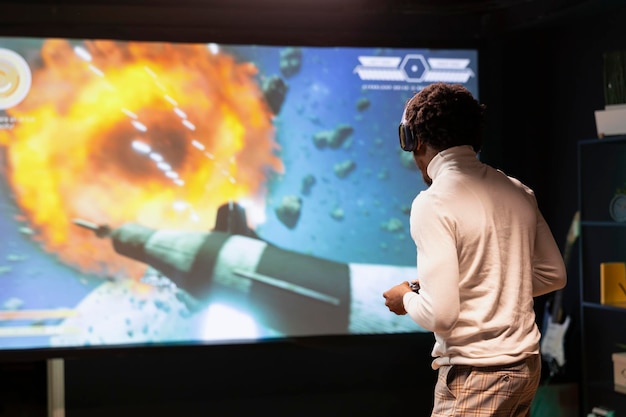 Free Photo man standing up in front of ultrawide screen playing videogame using controller