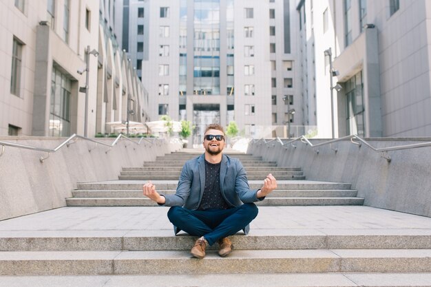 Man in sunglasses sitting on concrete stairs in meditation pose